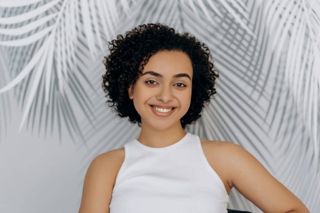 Smiling woman standing in front of a leafy green background, representing vitality and renewal through NAD+ therapy at Formula Wellness.